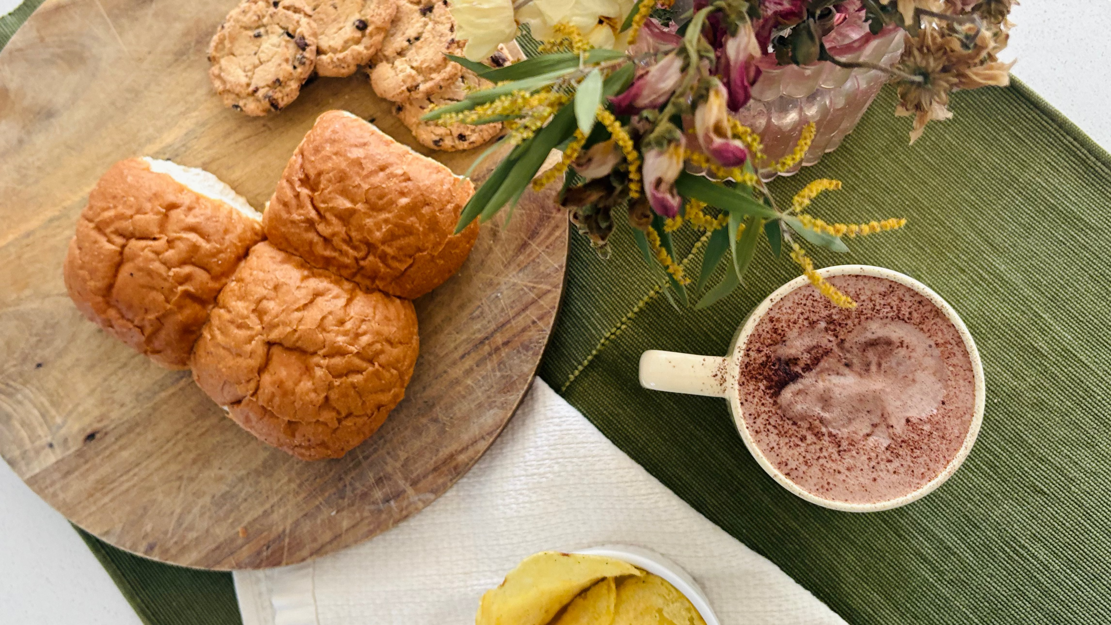 Wooden cutting board with croissants, a cup of coffee, and a bowl of chips on a green placemat.